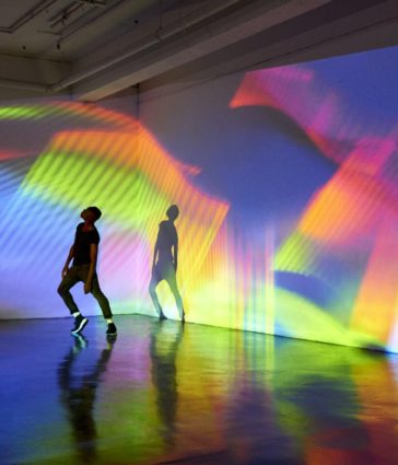Man dancing in front of large scale abstract image being projected onto the walls behind him
